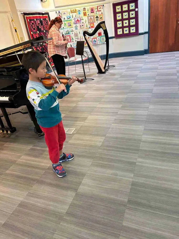 An Allegro Music School student plays the violin under the guidance of his teacher during the Winter Recital.
